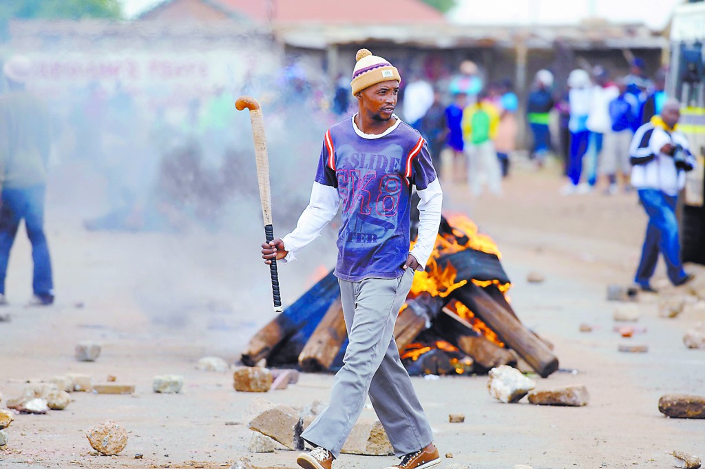 A Bekkersdal community member walks passed burning tyres during protest, 23 October 2013. Residents took to the streets after failed service delivery negotiations. Picture: Refilwe Modise