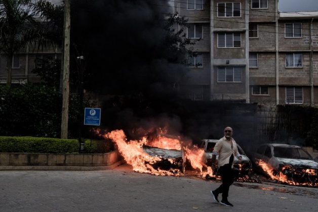 Graphic content / A man passes in front of burning cars that exploded at the entrance of DusitD2 hotel in Nairobi, Kenya, on January 15, 2019, after a blast followed by a gun battle rocked the upmarket hotel and office complex. (Photo by KABIR DHANJI / AFP)
