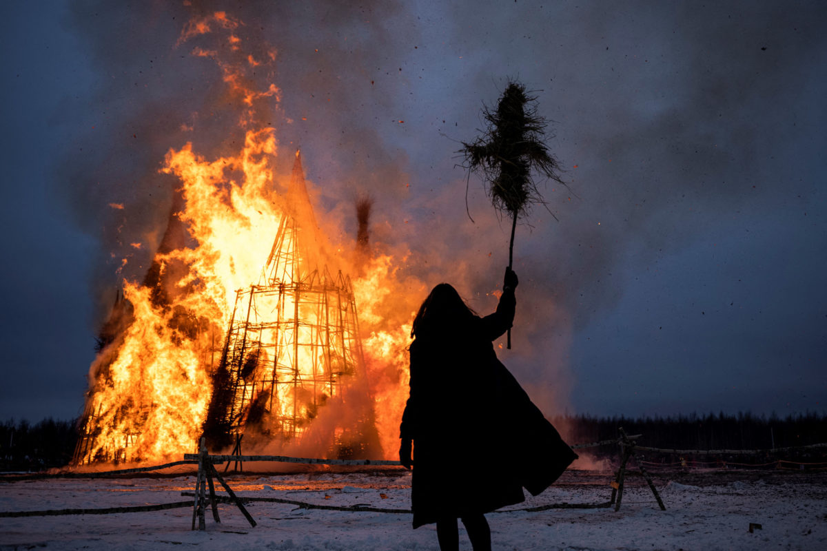 This picture taken on March 13, 2021, shows a spectator watching the burning wooden structure 'Corona Tower' created by Russian artist Nikolay Polissky during celebrations of Maslenitsa, the eastern Slavic Shrovetide in the village of Nikola-Lenivets. - Shrovetide or Maslenitsa is an ancient farewell ceremony to winter, traditionally celebrated in Belarus, Russia and Ukraine and involves the burning of a large effigy. (Photo by Dimitar DILKOFF / AFP)