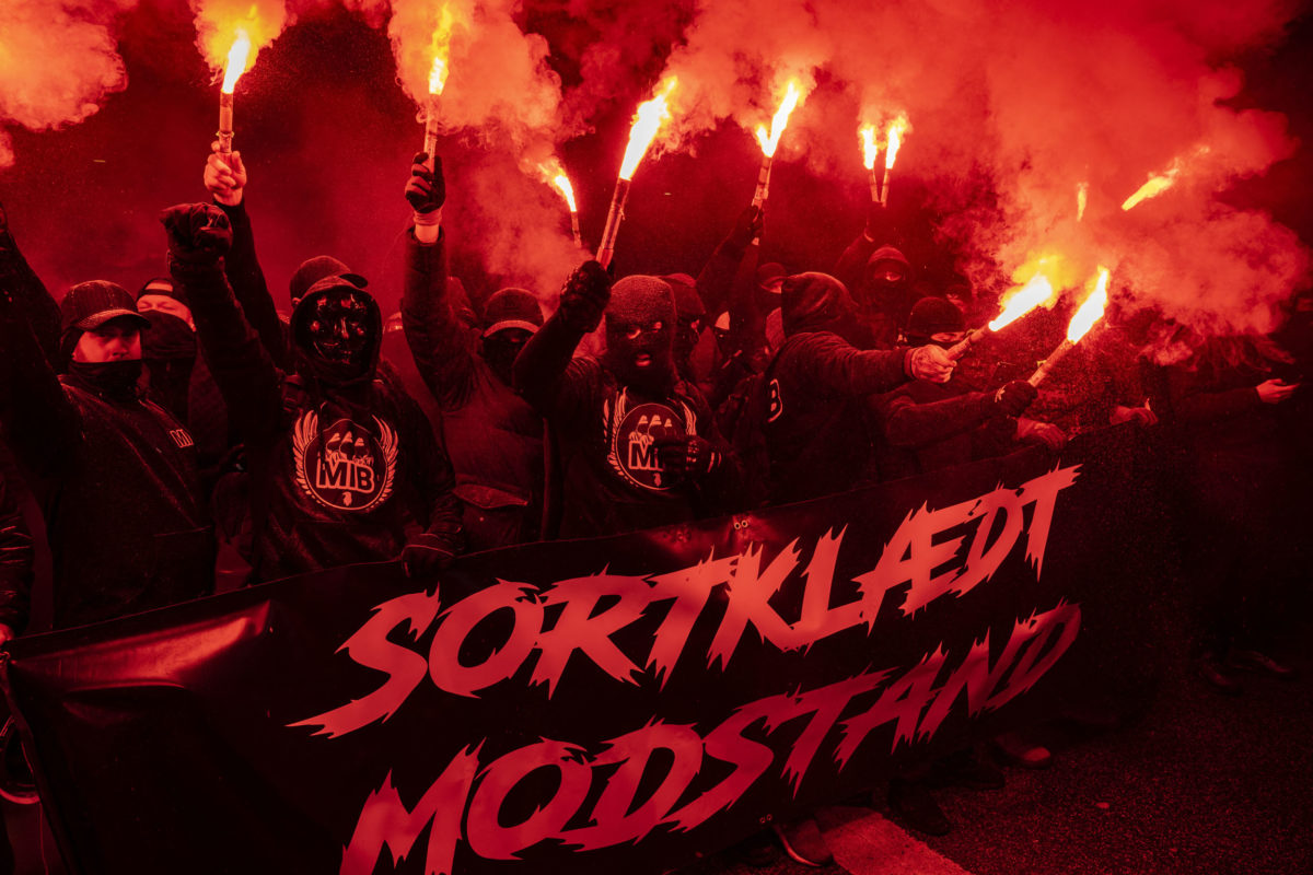 Supporters of the "Men in Black Denmark" movement stand behind a banner reading "Black-clad resistance" as they demonstrate against restrictions implemented to fight the spread of the novel coronavirus on March 13, 2021 in Copenhagen, Denmark. - Two people were arrested on the sidelines of a weekend protest against anti-coronavirus restrictions in Denmark's capital Copenhagen, the police said. (Photo by Martin Sylvest / Ritzau Scanpix / AFP) / Denmark OUT