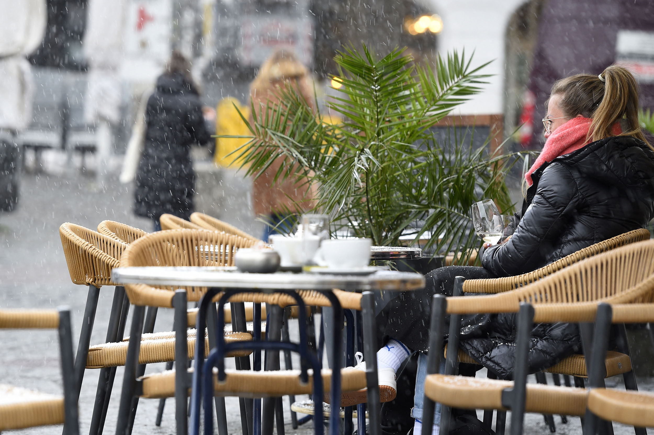 A woman takes a drink outside at a cafe during a sleet shower in Saarbruecken, western Germany, on April 6, 2021, as the border state of Saarland on Tuesday partially reopened during the ongoing coronavirus (Covid-19) pandemic. - Germans in the tiny border state of Saarland returned to cafes, cinemas and cultural venues on April 6, even as the rest of the country faces tighter coronavirus restrictions amid rising case numbers. (Photo by JEAN-CHRISTOPHE VERHAEGEN / AFP)