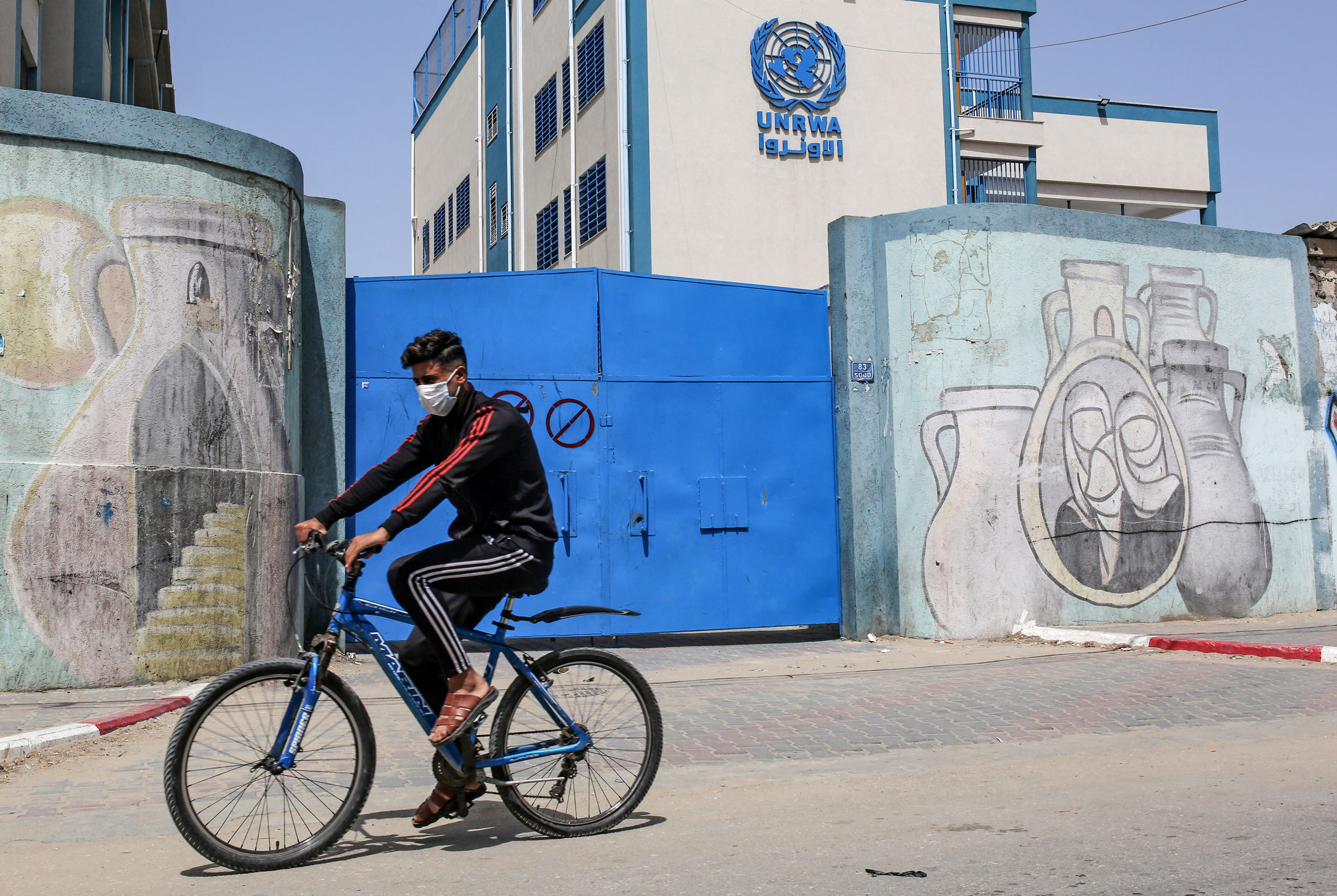 A Palestinian rides a bicycle past the closed gate of a school run by the United Nations Relief and Works Agency for Palestinian Refugees (UNRWA) in the city of Rafah in the southern Gaza Strip on April 6, 2021, amidst a lockdown due to the COVID-19 coronavirus pandemic. (Photo by SAID KHATIB / AFP)