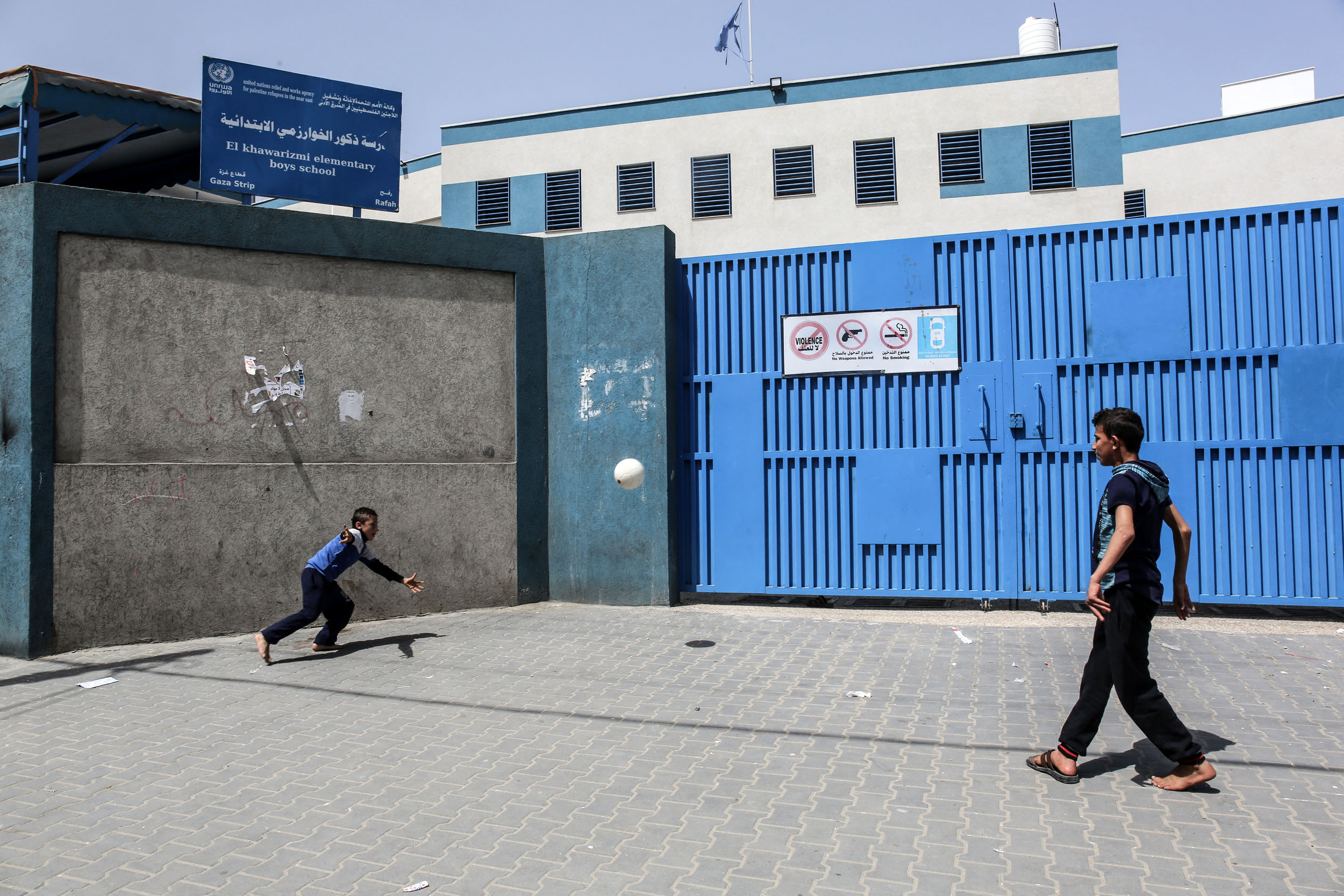 Children play with a football by the closed gate of a school run by the United Nations Relief and Works Agency for Palestinian Refugees (UNRWA) in the city of Rafah in the southern Gaza Strip on April 6, 2021, amidst a lockdown due to the COVID-19 coronavirus pandemic. (Photo by SAID KHATIB / AFP)