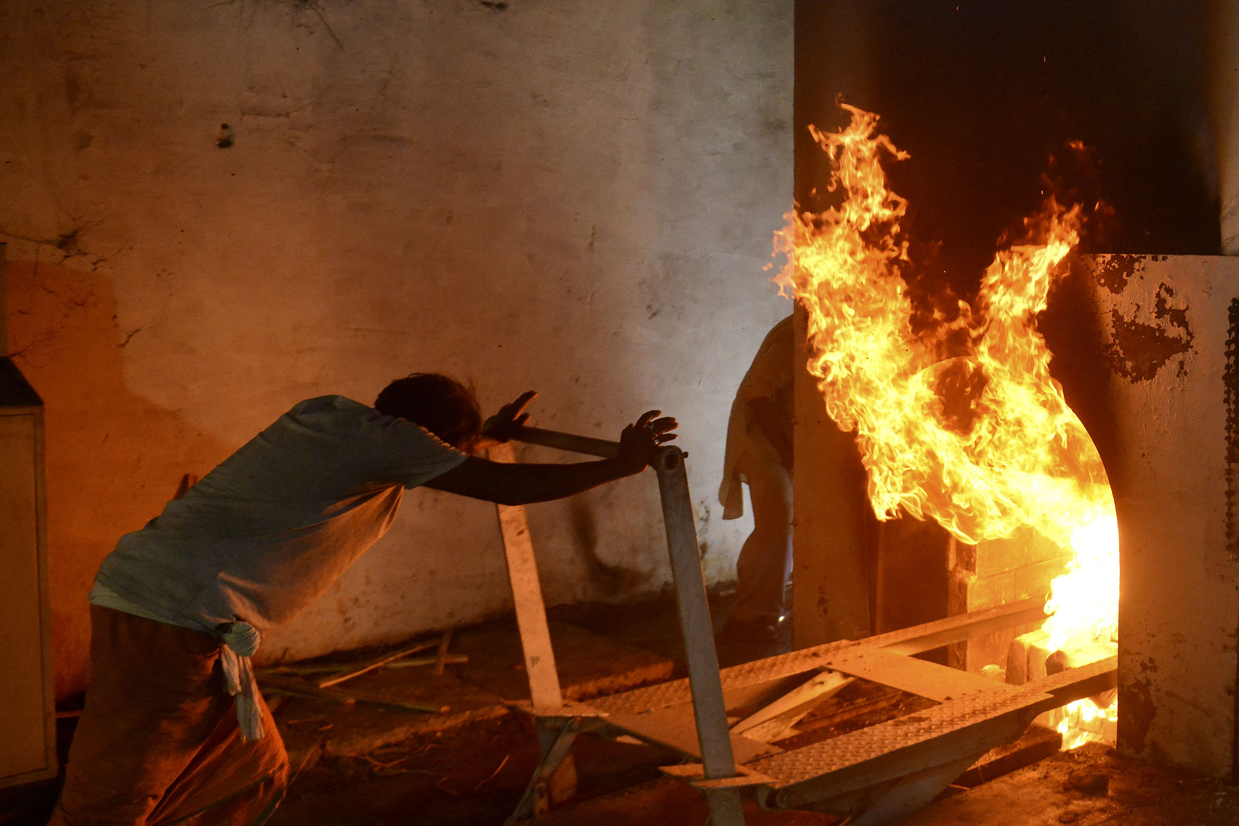 A worker pushes a trolley that carried the body of patient who died of the Covid-19 coronavirus into an furnace during the cremation at an electric crematorium in Allahabad on April 27, 2021. (Photo by SANJAY KANOJIA / AFP)