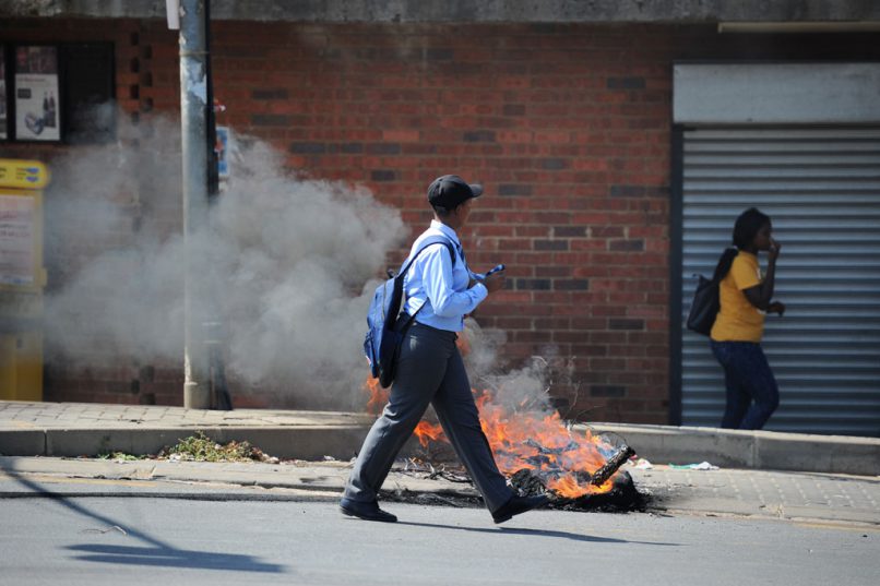 School pupils walk past burning tyres on New Canada Road in Noordgesig after residents blocked the road, 17 January 2018, in protest after Education MEC Panyaza Lesufi failed to arrive for a visit to Noordgesig Primary School. Police fired rubber bullets and teargas to disperse the crowd. A number of protesters and on-lookers were injured. Picture: Michel Bega